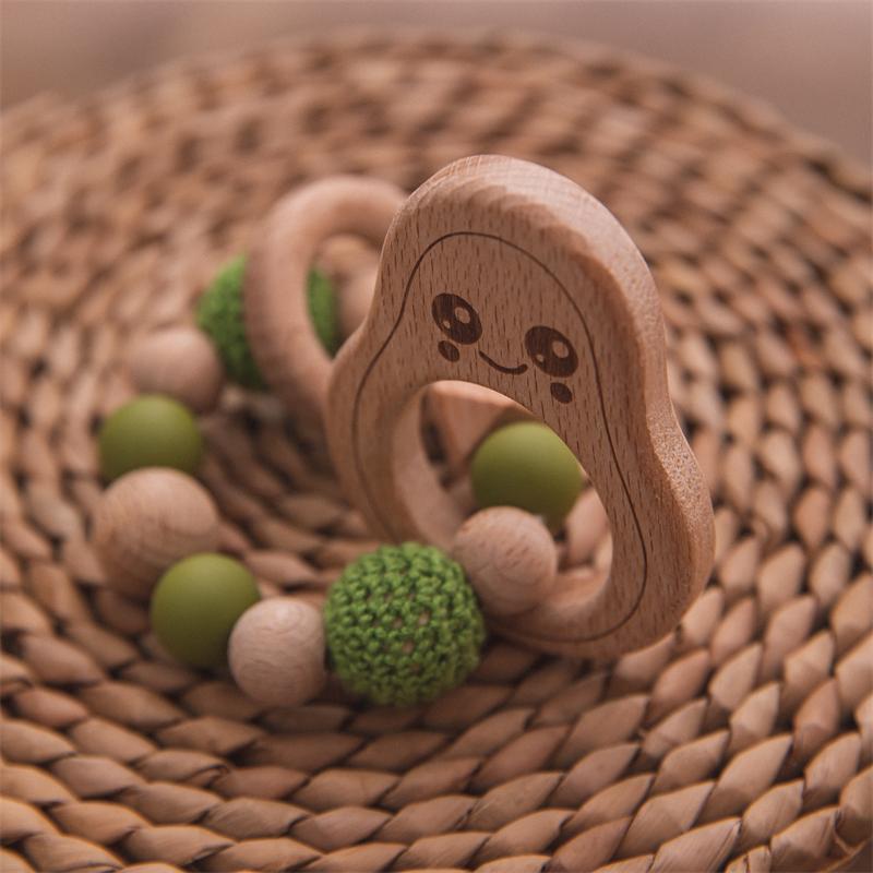 Wooden teething ring with green beads on a woven surface