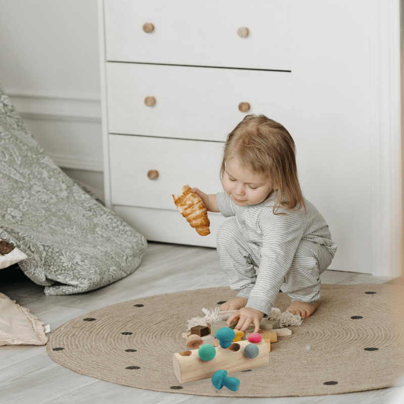 Child playing with a wooden toy on a rug in a room with white furniture.