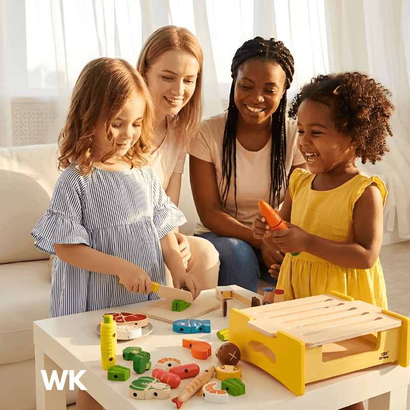 Two women and two young girls playing with toy kitchen set in a bright room.Tiny Grill Masters
