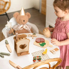 Child playing with wooden toys at a table, including a teddy bear and various play items.