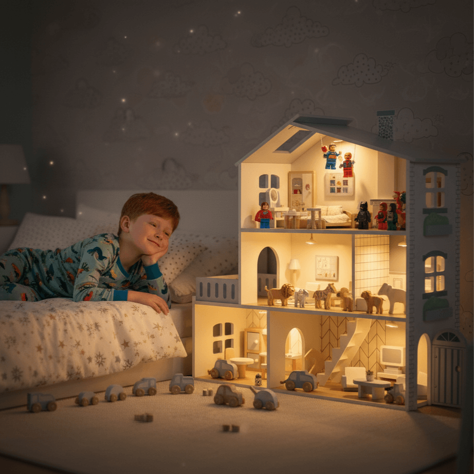 Child in pajamas lying on a bed next to a detailed dollhouse with lights on.Wooden Play House with Lights – Wonder Kiiids